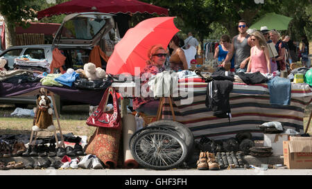 Ein Verkäufer bei einem Auto Boot Verkauf vide Grenier Unterstände unter einem Regenschirm oder Sonne Rotton auf einem glühend heißen Tag im Sommer in der Nähe von C Stockfoto