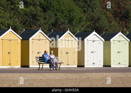 Bournemouth, Dorset, UK. 28. September 2016. Älteres paar sitzen auf Bank vor verschiedenen Schattierungen von gelb Strandhütten Promenade an einem herrlich warmen sonnigen Tag entspannen. Bildnachweis: Carolyn Jenkins/Alamy Live-Nachrichten Stockfoto