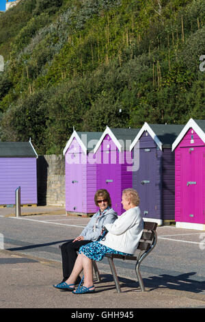 Bournemouth, Dorset, UK. 28. September 2016. Paar Frauen sitzen auf der Bank vor verschiedenen Schattierungen von lila Strandhütten Promenade an einem herrlich warmen sonnigen Tag entspannen. Bildnachweis: Carolyn Jenkins/Alamy Live-Nachrichten Stockfoto