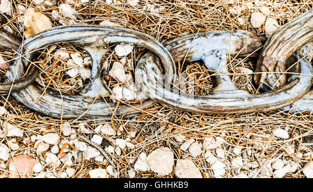 Extra große alte Kettenglieder auf Outdoor-Boden-Oberfläche mit Kieselsteinen und getrockneten Pflanzen. Stockfoto