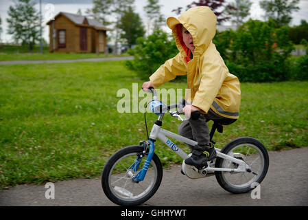 Ein kleiner Junge (4 Jahre alt) trägt einen gelben Regenmantel mit dem Fahrrad Stockfoto