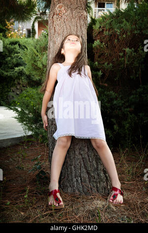 Kleines Mädchen lehnte sich gegen Baum, nachschlagen Stockfoto