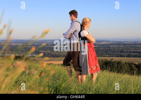 Ein deutsches Paar in bayerischer Tracht Rücken an Rücken auf dem Rasen Stockfoto