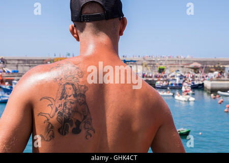 Einschiffung der Madonna, Nuestra Señora del Carmen auf einem Fischerboot beobachtet von einem jungen Mann mit Tattoo der Jungfrau und Stockfoto