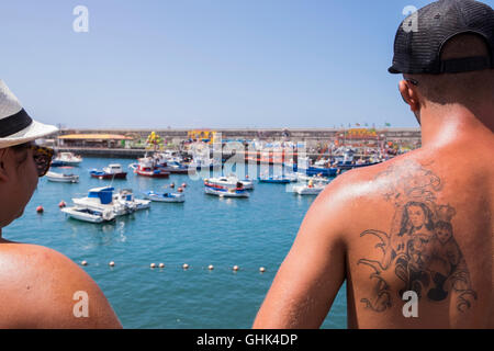 Einschiffung der Madonna, Nuestra Señora del Carmen auf einem Fischerboot beobachtet von einem jungen Mann mit Tattoo der Jungfrau und Stockfoto