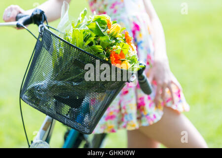 Junge Mädchen tragen ein Sommerkleid mit einem Blumenstrauß. Mit Fahrrad im park Stockfoto