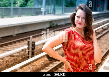 junge Frau im roten Kleid warten am Bahnsteig des Bahnhofs und lächelt Stockfoto