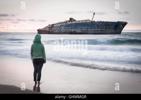 Eine Frau steht am Strand in der Nähe das Wrack der SS American Star, Fuerteventura, Kanarische Inseln, Spanien Stockfoto