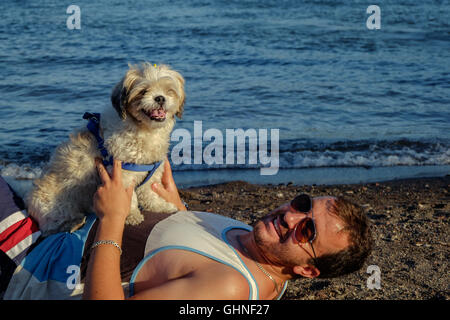 Ein Mann und ein Hund an einem Strand umarmt Stockfoto