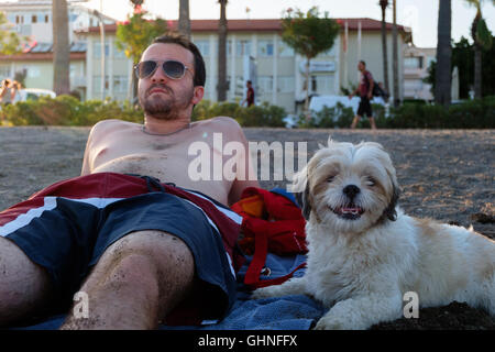 Ein Mann und ein Hund sitzt an einem Strand im Sommer Stockfoto