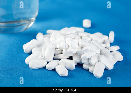 weiße Tabletten und ein Glas Wasser auf einem blauen Hintergrund Stockfoto