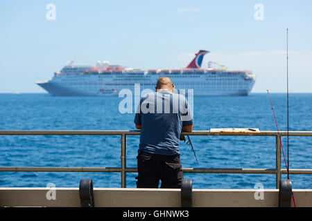 Mann Angeln vom Steg In Avalon, Catalina Island, Kalifornien. Das Kreuzfahrtschiff Carnival Inspiration verankert vor der Küste. Stockfoto