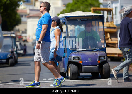 Paar überqueren Sie die Straße In Avalon, Santa Catalina Island. Eine malerische Insel-Golf-Cart wartet an der Kreuzung. Stockfoto