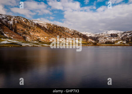 Watendlath Tarn in der Seenplatte, umgeben von Schnee bedeckt Fells an einem Spätnachmittag im März. Stockfoto