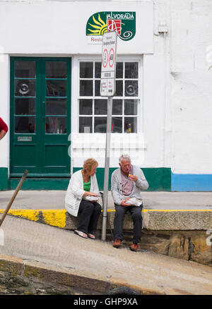 Ein Mann und eine Frau Essen Fisch und Chips auf den Hafen von Mevagissey, Cornwall, England, UK Stockfoto