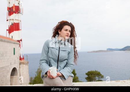 Junge Frau nimmt sich eine Auszeit mit Leuchtturm im Hintergrund Stockfoto