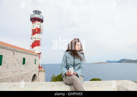 Junge Frau nimmt sich eine Auszeit mit Leuchtturm im Hintergrund Stockfoto