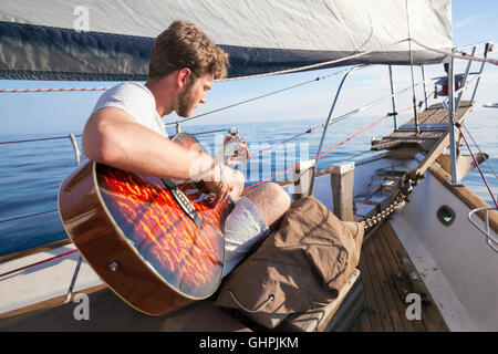 Junger Mann, die Gitarre auf Segelboot Stockfoto