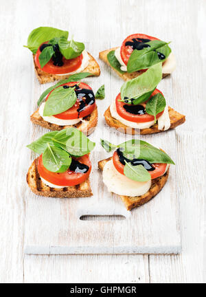 Caprese-Sandwiches mit Tomaten, Mozzarella, Basilikum und Balsamico-Glasur auf gemalte Tafel in hellem Holz Hintergrund Stockfoto