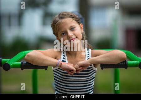 Porträt von kleinen Mädchen sitzen auf Fitnessgeräten im öffentlichen Park. Stockfoto