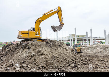 Gelbe Bagger macht Flor des Bodens durch Hochziehen Boden auf Heap auf Baustelle, Projekt im Gange. Stockfoto