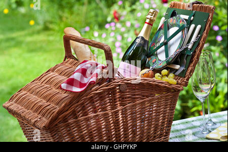 Englischer Sparkling Rosé Weinflasche und Weidenkorb Picknickkorb Korb Korb Baguette Trauben Obst in sonniger floraler UK Garten Situation Stockfoto