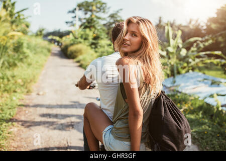 Hintere Ansicht Schuss attraktive junge Frauen sitzen auf Rückseite ihr Freund Reiten Fahrrad auf Landstraße. Stockfoto