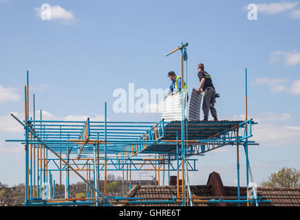 Bauherren tragen Wellblech Blätter stehen auf Gerüsten über Dach des Reihenhaus in Nord-London Stockfoto