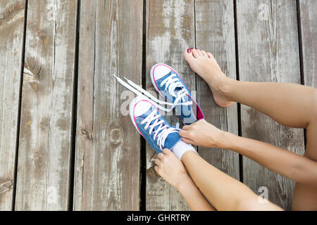 Junge Frau binden Schnürsenkel ihrer Jeans Sneaker sitzt auf dem Holzboden Stockfoto