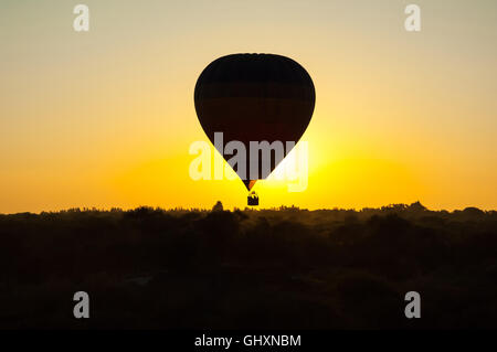 Silhouette der Heißluftballon in wolkenlosen Himmel bei Sonnenaufgang über nebligen afrikanische Ebene Stockfoto