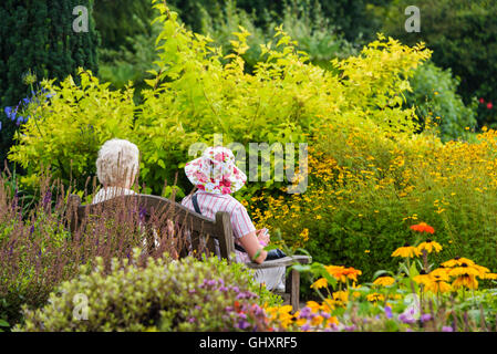 Zwei ältere Damen entspannenden unter den bunten Blumenrabatten. Stockfoto