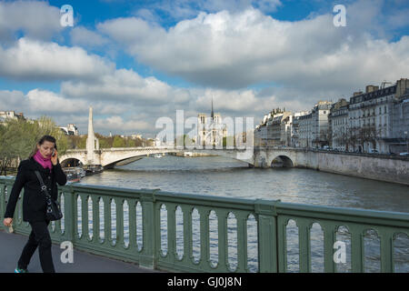 eine Frau auf ihrem Handy auf der Pont de Sully mit der Île De La Cité über Paris, Frankreich Stockfoto