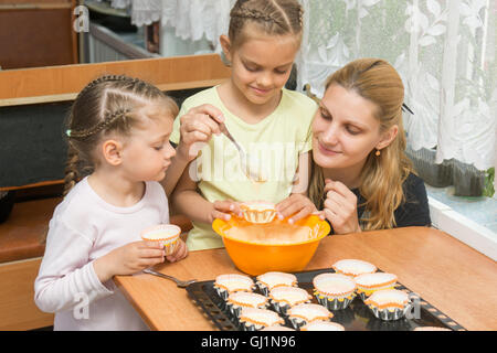 Die ältere Tochter schüttet Teig für Kuchen in Dosen unter der Obhut meiner Mutter und Schwester Stockfoto