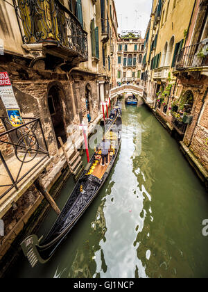 Gondeln mit Gondoliere im traditionellen Gestreifte Oberteile, auf einem schmalen Kanal in Venedig festgemacht. Italien. Stockfoto