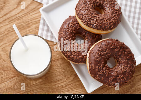 Glas Milch und Schokolade Donuts auf Holztisch Stockfoto