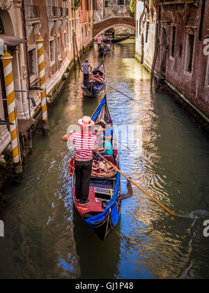 Gondoliere tragen traditionelle gestreiften Oberteil und Strohhut Hut Lenkung seine Gondel entlang einer schmalen Kanal in Venedig, Italien. Stockfoto