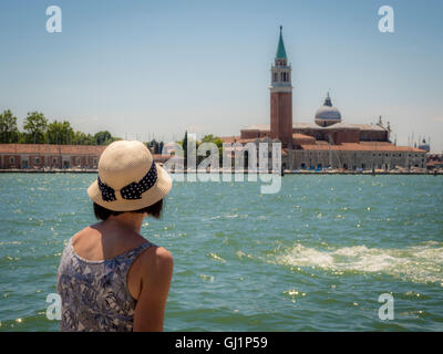 Rückansicht des einzigen Weibchen, mit Stroh Hut, sitzt auf einer Bank Blick auf die Kirche und die Insel San Giorgio Maggi Stockfoto