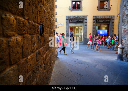 Fußgänger leiten eine Filiale der Bank Monte dei Paschi di Siena Via Banchi di Sopra in Siena, Italien. Stockfoto