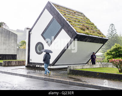 Haus im Regen auf den Kopf. Ein Mann mit einem Regenschirm geht durch das invertierte Haus (das ist wirklich ein Transformator). Stockfoto