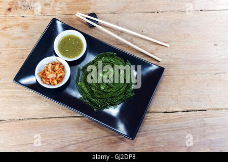 Meer Trauben oder grünen Kaviar und pikanter Sauce auf einem schwarzen Schale der Holztisch Stockfoto