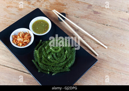 Meer Trauben oder grünen Kaviar und pikanter Sauce auf einem schwarzen Schale der Holztisch Stockfoto