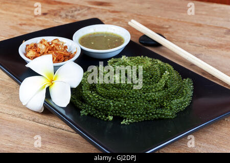 Meer Trauben oder grünen Kaviar und pikanter Sauce auf einem schwarzen Schale der Holztisch Stockfoto