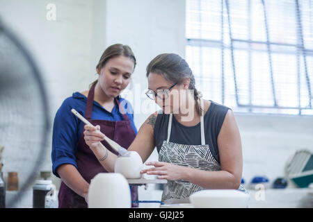 Weiblichen Auszubildenden zeigt, wie Sie im Workshop Glasur potter Stockfoto