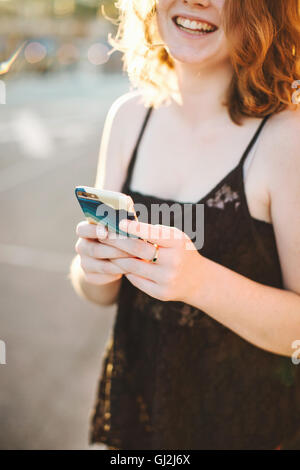Blick auf rote kurzhaarige Frau hält Smartphone lächelnd beschnitten Stockfoto
