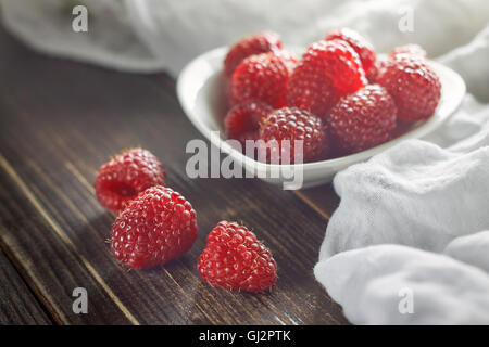 Rote Himbeeren in weiße Schüssel auf Holzuntergrund Stockfoto