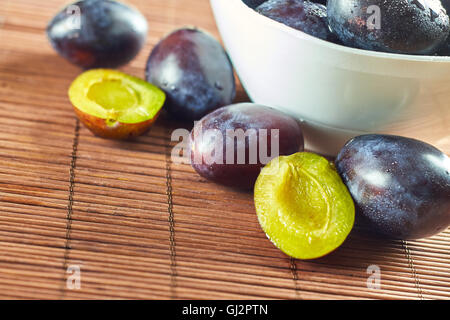 Frische Zwetschgen in Schüssel auf hölzernen Hintergrund weiß. Textfreiraum Stockfoto