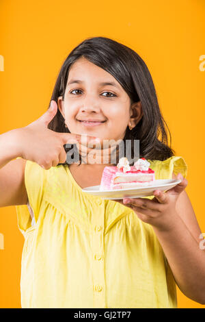 Porträt der indischen Kind essen, Kuchen oder Gebäck, niedliche kleine Mädchen essen Kuchen, Mädchen essen Schokolade Kuchen über farbigen Hintergrund Stockfoto