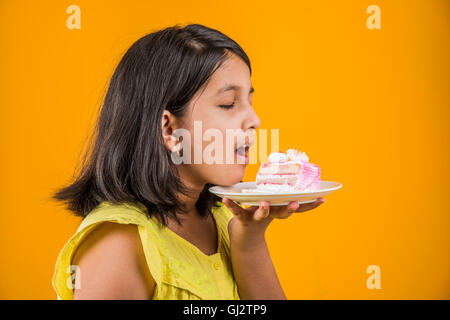 Porträt der indischen Kind essen, Kuchen oder Gebäck, niedliche kleine Mädchen essen Kuchen, Mädchen essen Schokolade Kuchen über farbigen Hintergrund Stockfoto