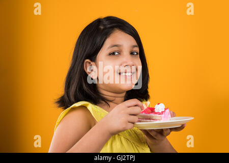 Porträt der indischen Kind essen, Kuchen oder Gebäck, niedliche kleine Mädchen essen Kuchen, Mädchen essen Schokolade Kuchen über farbigen Hintergrund Stockfoto