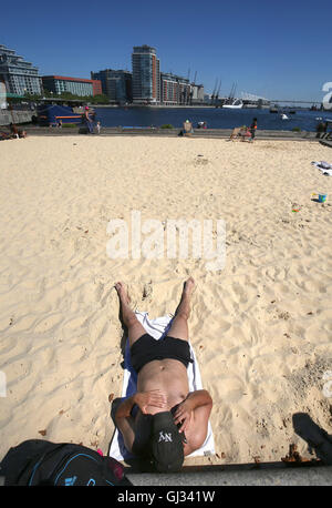 Ein Mann sonnt sich am Strand Urban London in den Royal Docks in London. Stockfoto